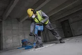 Une personne portant un équipement de sécurité démolit un sol en béton à l'aide d'un marteau de démolition.
