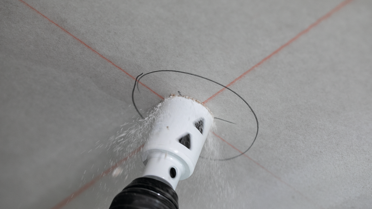 Une scie cloche découpe une ouverture circulaire dans les cloisons sèches, guidée par des lignes laser croisées.