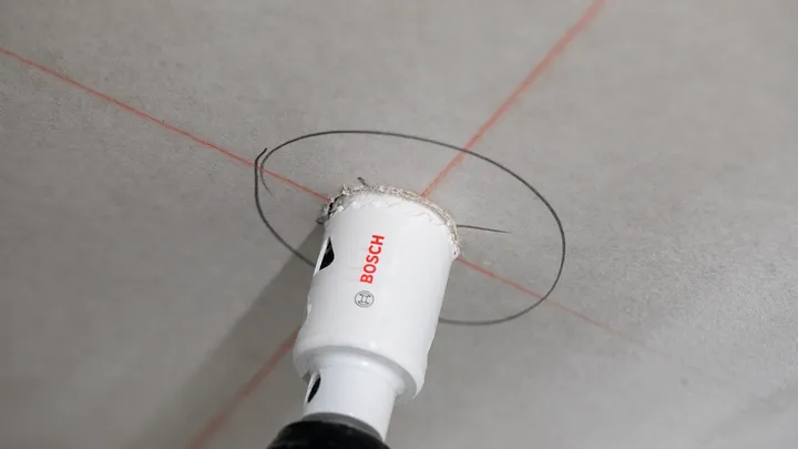 Scie cloche découpant une ouverture circulaire dans un plafond marquée par des lignes de guidage.