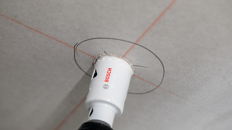 Scie cloche découpant une ouverture circulaire dans un plafond marquée par des lignes de guidage.