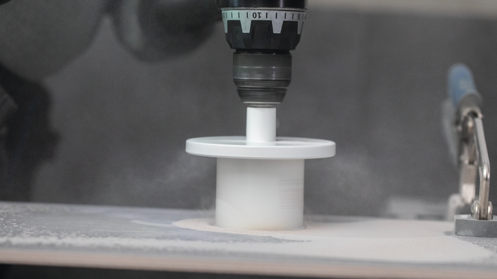 Une perceuse équipée d'une scie cloche coupe une surface plane.