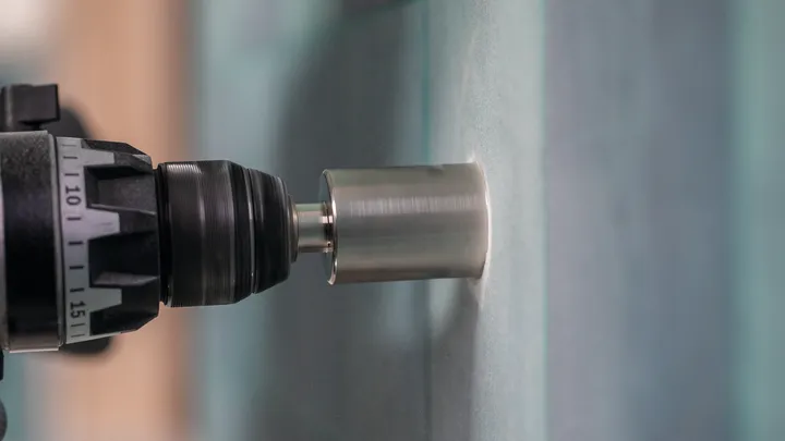 Une perceuse avec une scie cloche coupant un panneau de verre.