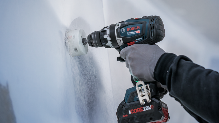 Une personne portant un équipement de sécurité perce un grand trou dans un mur blanc.