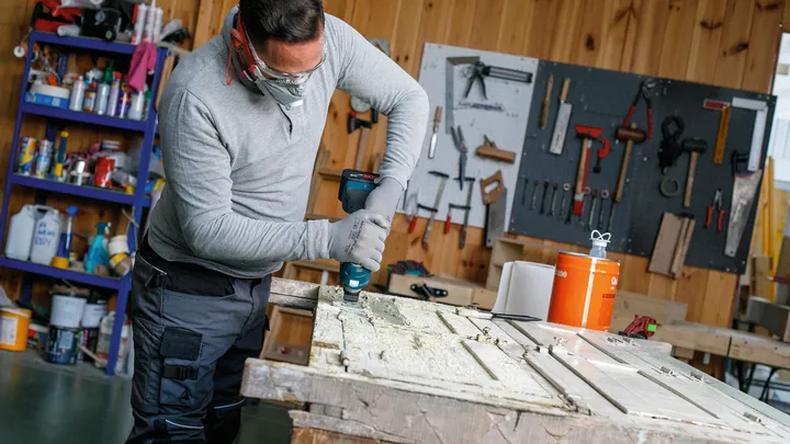 Une personne portant un équipement de sécurité perce une porte en bois dans un atelier.