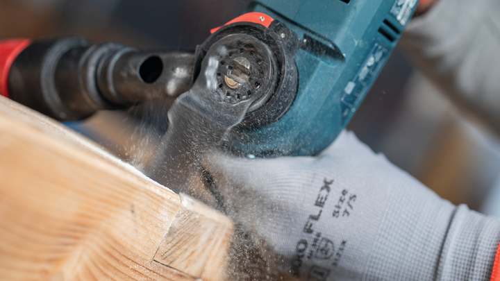 Une personne portant un équipement de sécurité perce une poutre en bois, créant de la sciure.