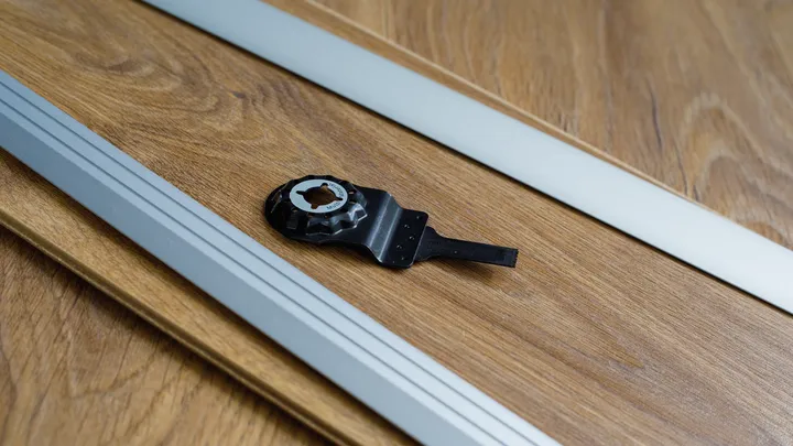 Lame d'outil oscillant sur une surface en bois à côté de deux guides en aluminium.