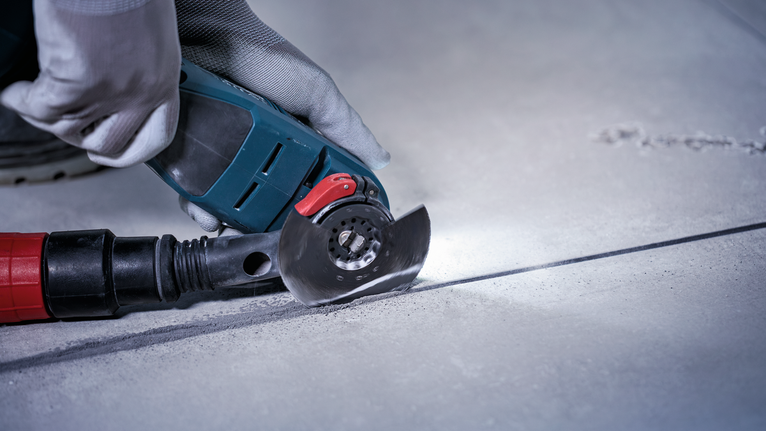 Une personne portant un équipement de sécurité découpe du béton avec un outil électrique.