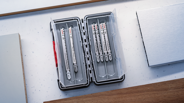 Lames de scie sauteuse organisées dans un boîtier en plastique sur un plan de travail.