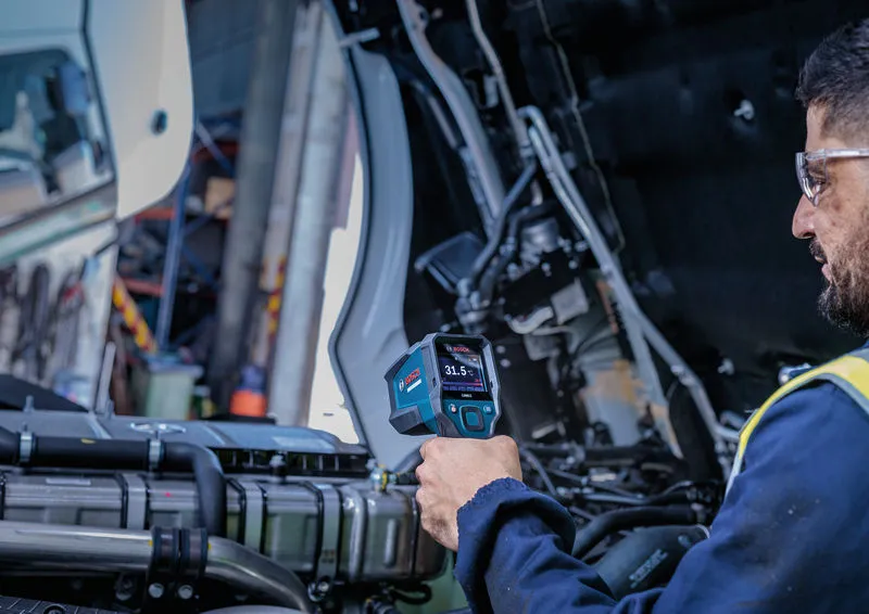 Une personne portant un équipement de sécurité utilise un détecteur thermique pour mesurer la température dans le compartiment moteur.