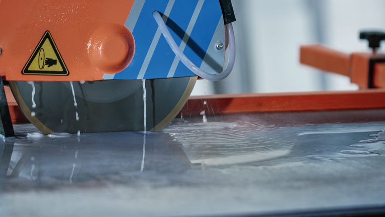 Scie à eau pour carrelage coupant une dalle tandis que l'eau refroidit la lame.