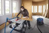 Une personne portant un équipement de sécurité coupe du bois sur une scie circulaire dans un atelier.