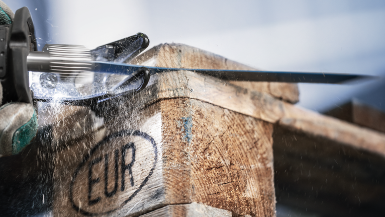 Une personne portant un équipement de sécurité découpe une palette en bois avec une scie alternative.