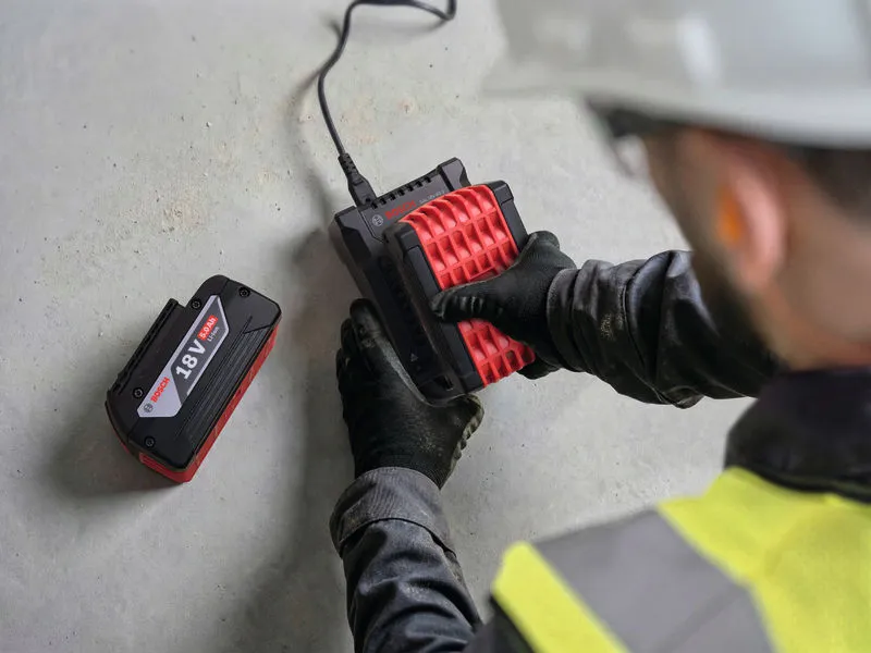 Une personne portant un équipement de sécurité branche une batterie à un chargeur sur une surface en béton.