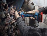 Une personne portant un équipement de sécurité utilise une meuleuse droite sans fil sur des machines métalliques.