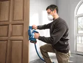 Une personne portant un équipement de sécurité utilise une raboteuse sans fil sur une porte en bois.