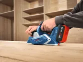 Dans un atelier, une personne lisse une surface en bois à l'aide d'une raboteuse sans fil.