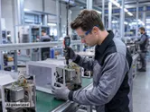 Une personne portant un équipement de sécurité assemble des appareils électroménagers à l'aide d'un outil électrique sur une chaîne de production.