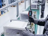 Une personne portant un équipement de sécurité assemble un four à micro-ondes sur une chaîne de production en usine.