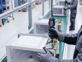 Une personne portant un équipement de sécurité utilise un outil électrique pour assembler des appareils électroniques sur une chaîne de production.