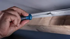 Une personne utilise un tournevis pour fixer une vis dans un rail métallique fixé au bois.