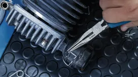 Une personne utilise une pince à bec fin pour ajuster une pièce métallique sur une machine.