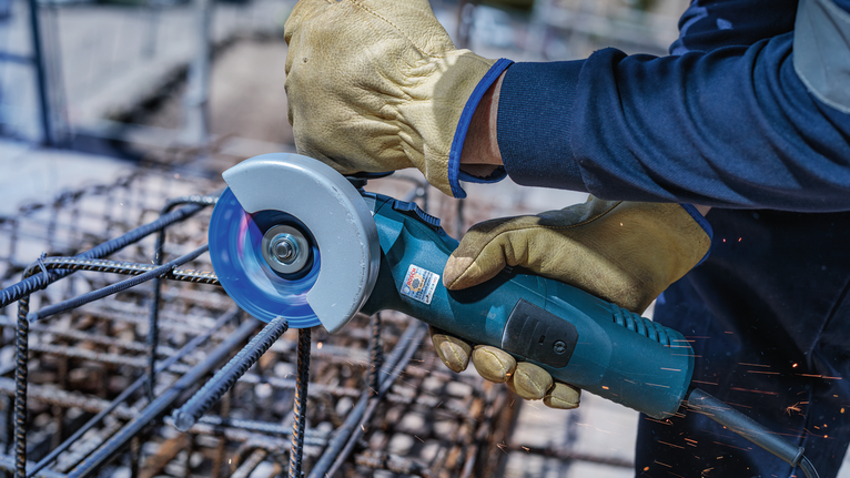 Une personne portant un équipement de sécurité utilise une meuleuse d'angle pour couper des barres d'armature métalliques.