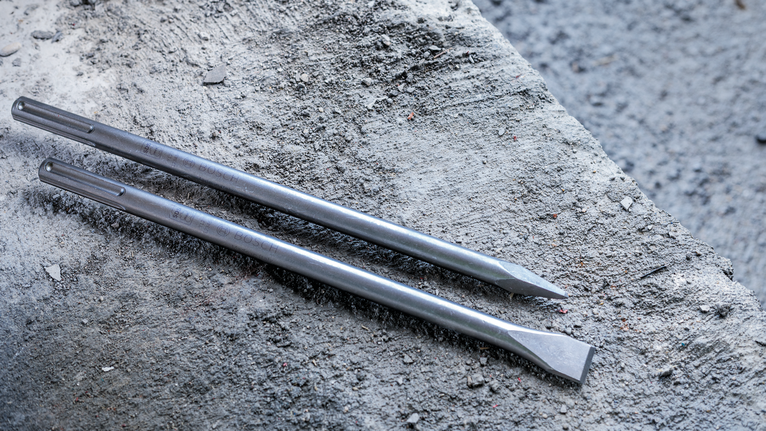 Deux mèches de burin en acier reposent sur du béton brut.
