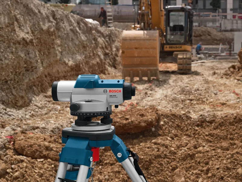 Outil de nivellement laser sur un trépied sur un chantier de construction à proximité d'une excavatrice.