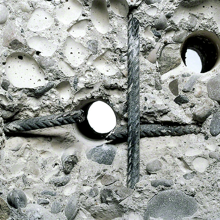 Trous percés croisant des barres d'armature métalliques à l'intérieur d'une dalle de béton brute.