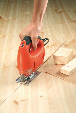 Una persona usa un seghetto alternativo per tagliare una tavola di legno seguendo una linea retta.