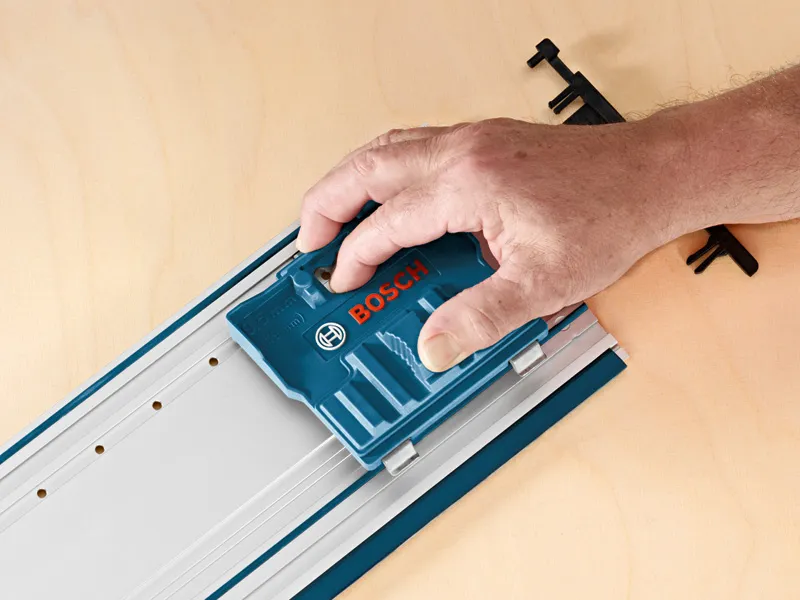 Una persona utilizza un accessorio di sistema blu su una rotaia metallica posta su una superficie di legno.