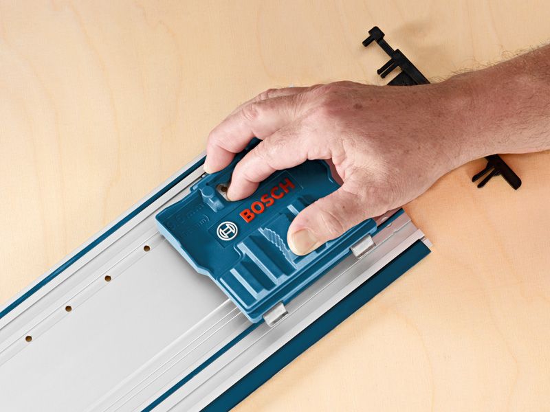 Una persona utilizza un accessorio di sistema blu su una rotaia metallica posta su una superficie di legno.