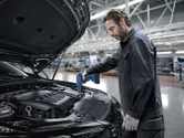 Una persona che indossa un equipaggiamento di sicurezza utilizza una pistola termica su una catena di montaggio di automobili.