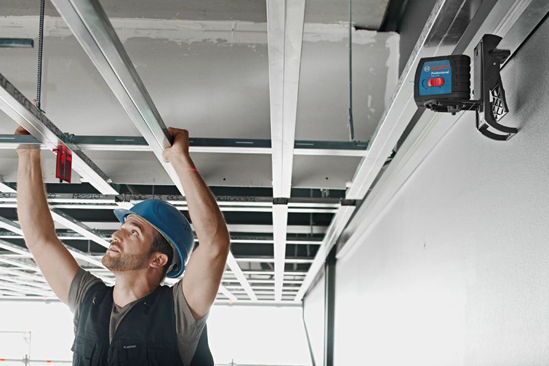 Una persona che indossa dispositivi di sicurezza allinea i telai del soffitto utilizzando uno strumento di livellamento laser.