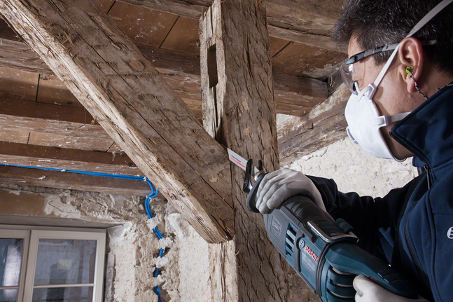 Un operaio che indossa dispositivi di sicurezza taglia una trave di legno utilizzando un seghetto alternativo.