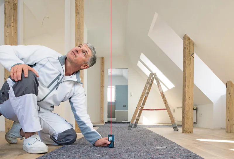 Una persona utilizza un misuratore laser per controllare l'allineamento verticale in una luminosa soffitta.