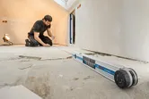 Una persona è inginocchiata su un pavimento di un cantiere edile e utilizza un misuratore d'angolo con una linea laser rossa.