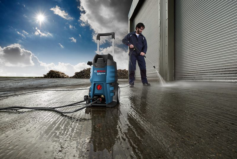 Una persona che indossa un equipaggiamento di sicurezza utilizza un'idropulitrice per pulire il pavimento in cemento bagnato.