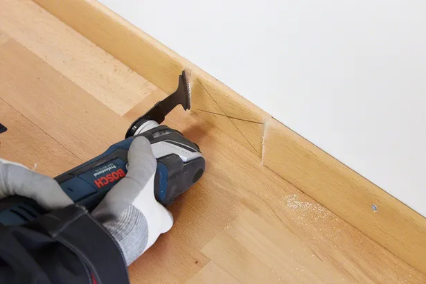 Una persona che indossa un equipaggiamento di sicurezza taglia uno zoccolo di legno con un utensile multiuso.