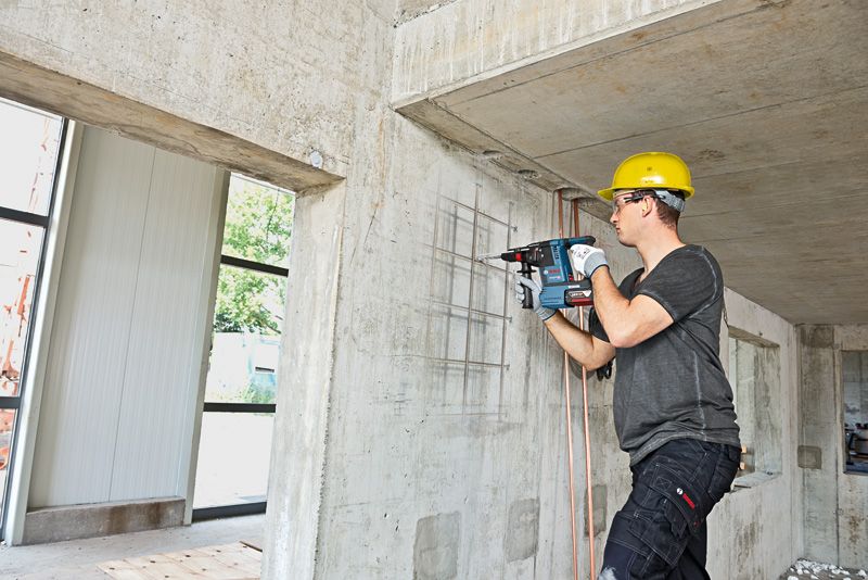 Una persona che indossa un equipaggiamento di sicurezza perfora un muro di cemento utilizzando un martello perforatore.
