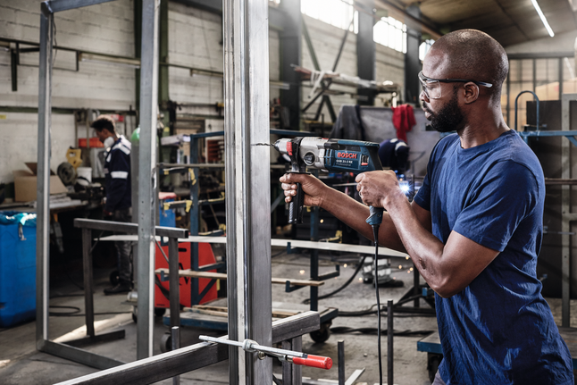 Una persona che indossa dispositivi di sicurezza perfora un telaio metallico in un'officina industriale.