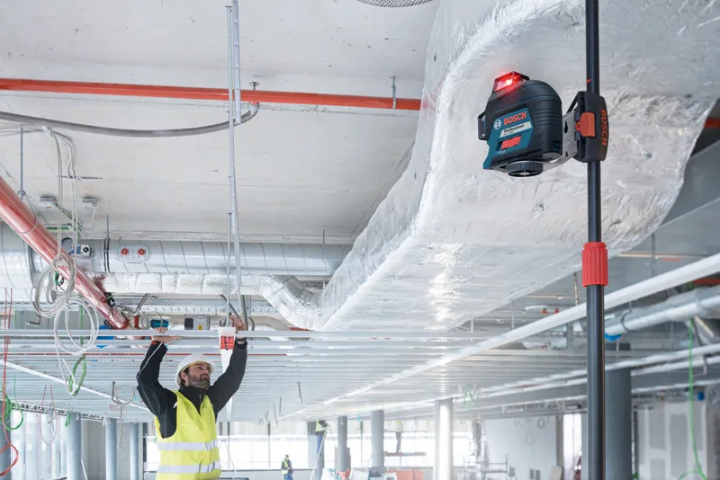 Una persona che indossa dispositivi di sicurezza allinea i telai del soffitto utilizzando uno strumento di livellamento laser.