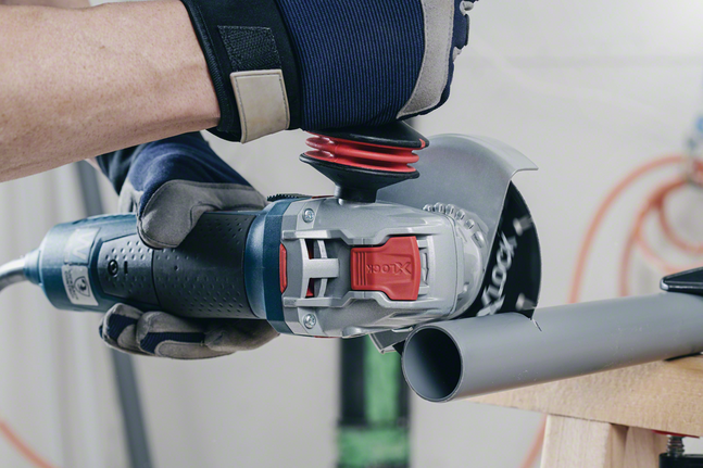 Una persona che indossa un equipaggiamento di sicurezza utilizza una smerigliatrice angolare per tagliare un tubo di plastica.