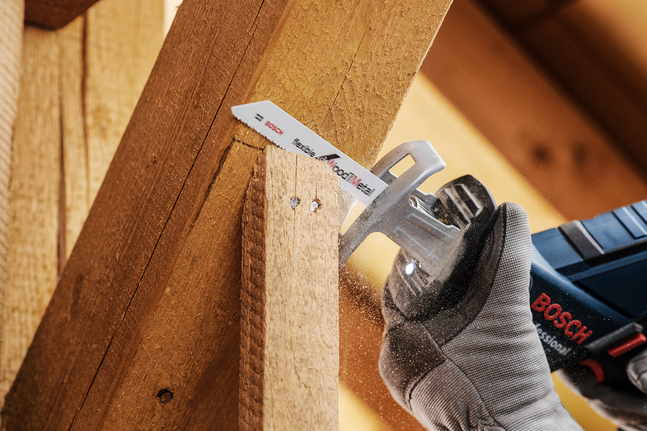 Una persona con indosso dispositivi di protezione individuale taglia una trave di legno con una sega alternativa.