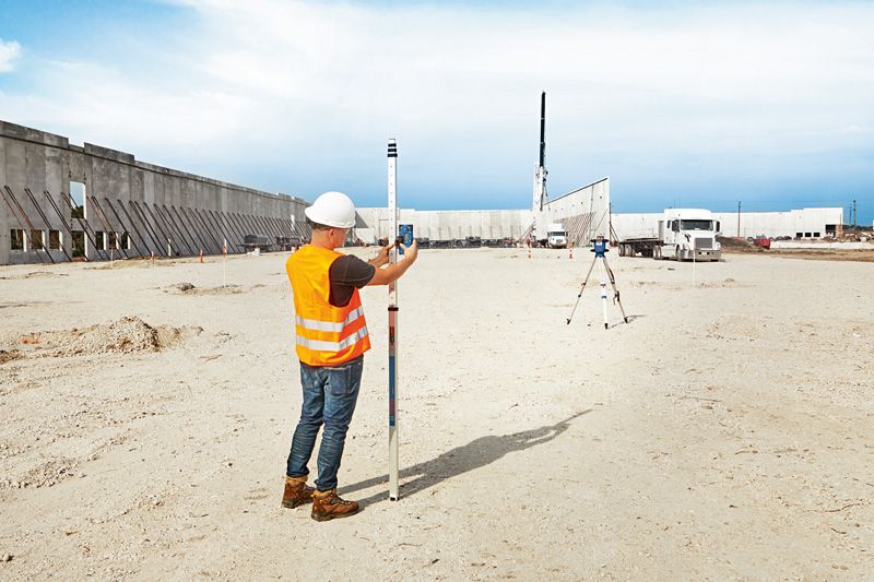 Persona che indossa dispositivi di sicurezza mentre allinea un ricevitore laser con uno strumento di livellamento laser in un cantiere edile.