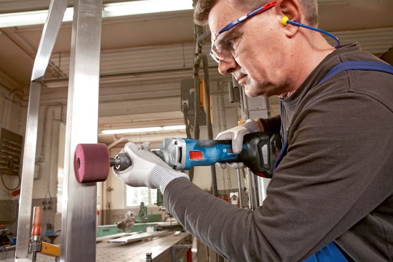 Una persona che indossa un equipaggiamento di sicurezza utilizza una smerigliatrice dritta senza fili su una trave di acciaio.