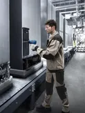 Una persona che indossa un equipaggiamento di sicurezza utilizza un elettroutensile per ispezionare le attrezzature su una catena di montaggio.