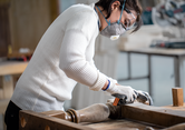 Una persona che indossa dispositivi di sicurezza leviga la gamba di un tavolo in legno in un'officina.