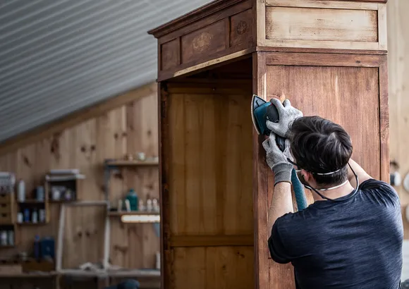 Persona che indossa dispositivi di sicurezza mentre leviga un mobile in legno in un'officina.