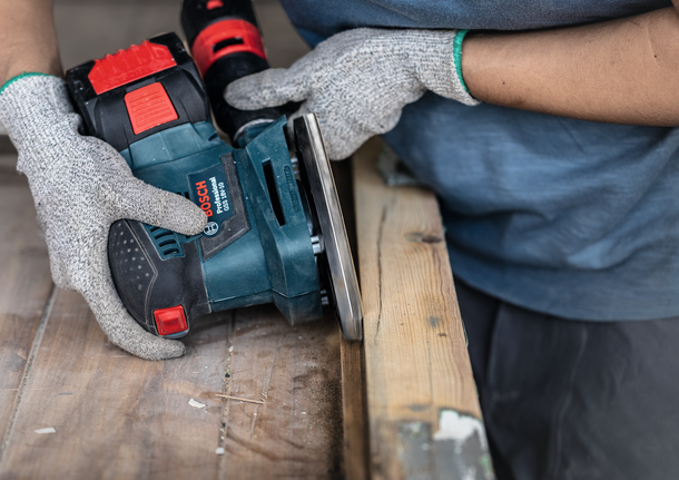 Una persona che indossa dispositivi di sicurezza leviga una superficie di legno con un utensile elettrico.